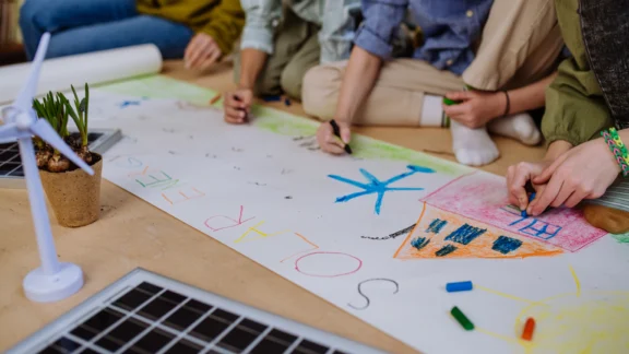 Kinder zeichnen gemeinsam ein großes Panoramabild. Darauf sind Häuser und Windkraftanlagen zu sehen. Die Überschrift lautet Solarenergie.