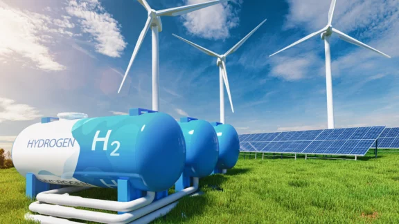 Wasserstofftanks stehen auf einer grünen Wiese. Hinter ihnen stehen Windräder und Solarzellen.